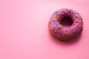 Fototapeta na wymiar Homemade circle donut with pink icing and rainbow sprinkles on the trendy soft pink background situated on the right side. Free copy space. Doughnut pastry.