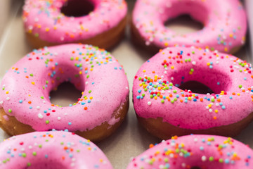 Homemade circle donuts with pink icing and rainbow sprinkles in white box on craft paper background. Doughnut pastry. Close up macro shoot