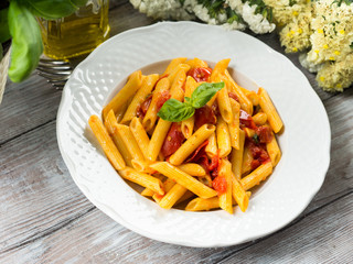 Penne pasta with fresh tomatoes and basil on wooden table. Traditional italian dish