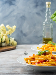 Penne pasta with fresh tomatoes and basil on wooden table. Traditional italian dish