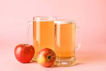 Mugs of apple cider on color background