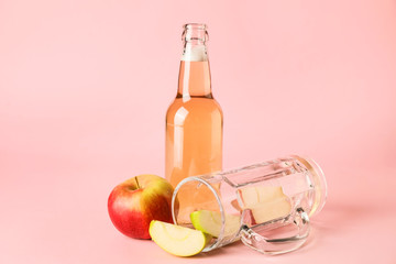Bottle of apple cider and mug on color background