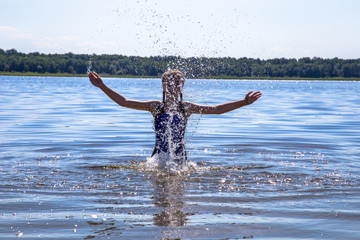 happy young girl jumping in a lake and spraying water around herself with her hands.