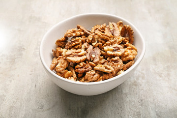 Bowl with tasty walnuts on light background