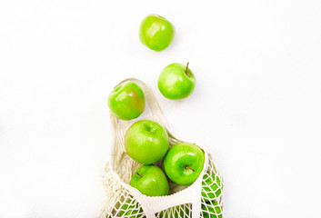 Organic green apples in reusable eco-friendly string mesh bag. Zero waste, plastic free and sustainable lifestyle concept. White kitchen table background, copy space, top view