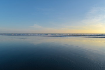 Tasman Sea horizon and faint clouds reflecting in thin water film over black sand in evening light