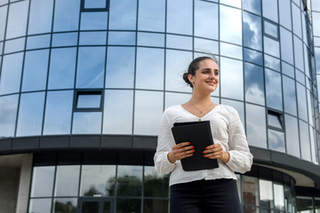 Fototapeta premium Portrait of beautiful woman with tablet outdoors near big office center