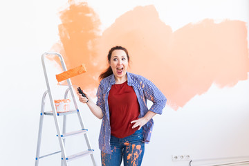 Dancing funny young woman painting wall in her new apartment. Renovation, redecoration and repair concept.