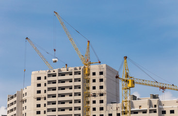Fototapeta na wymiar Construction site. Unfinished apartment buildings. Construction workers laying bricks on top. Special industrial cranes in the middle. Blue sky background.