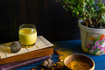 Golden milk powder and a glass with golden milk, on a blue table.