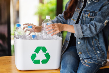 A woman collecting and separating recyclable garbage plastic bottles into a trash bin at home