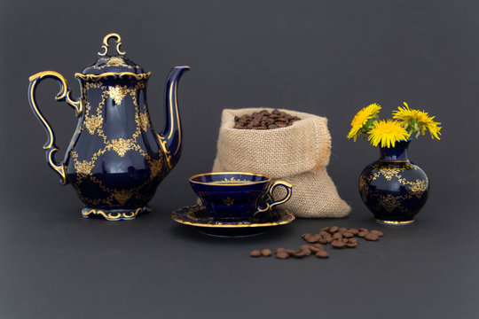 Still life with a beautiful cobalt blue colored vintage porcelain coffee set with golden floral pattern, a flower vase and a gunnysack filled with roasted coffee beans.