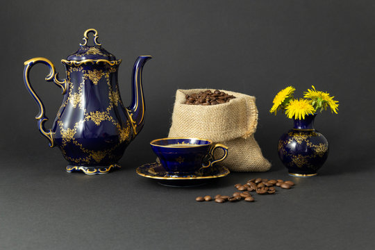 Still life with a beautiful cobalt blue colored vintage porcelain coffee set with golden floral pattern, a flower vase and a gunnysack filled with roasted coffee beans.