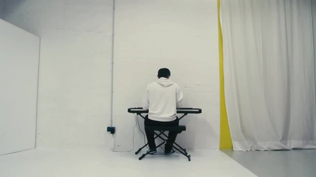 Person in a white hoodie playing on an electric keyboard. Detail shot of a talented pianist playing piano on a cheep keyboard in a studio.