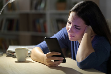 Sad woman complaining checking phone at night at home