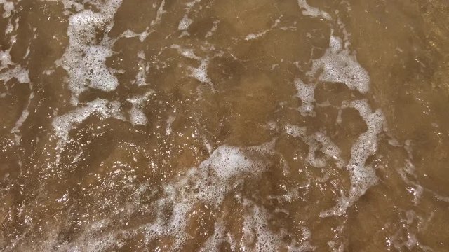 Crystal clear transparent water splashes on shoreline sandy beach, handheld close up