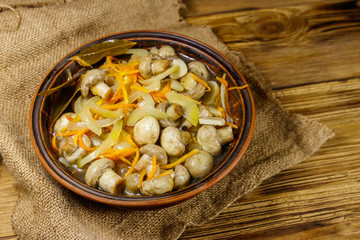 Delicious marinated mushrooms with carrot, onion and spices in ceramic bowl on wooden table
