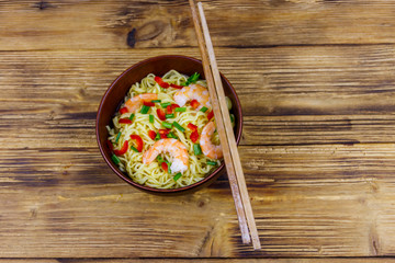 Bowl of instant Chinese noodles with shrimps, green onion and red hot chilli peppers on wooden table. Top view