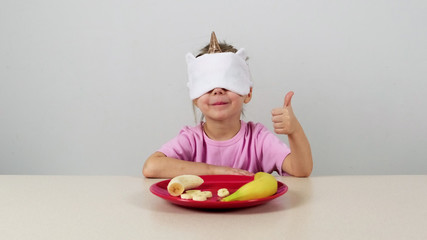 Little girl in a mask tries and guesses banan and gives thumbs up