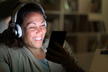 Happy adult woman listens music on phone at night at home