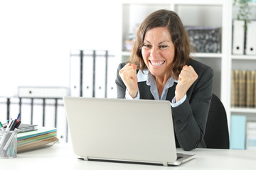Excited adult executive celebrating news on laptop at office