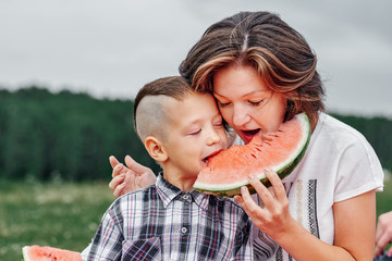 Mother and son eating watermelon in meadow or park. Happy family on picnic. outdoor portrait Little boy and mom