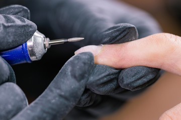 Process manicure close-up. Preparation for hardware manicure. Beautician in rubber gloves cuts the cuticle and processes nails.