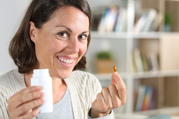 Adult woman showing vitamin pill looking camera at home