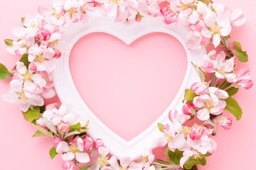 Frame of white heart shape and apple blossoms on light pink table background. Pastel color. Love...