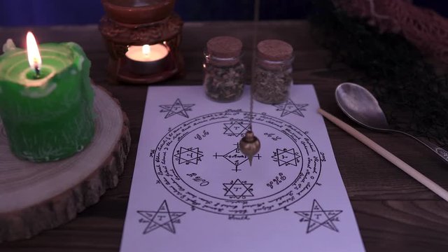 Witchcraft and wizardry. The sorcerer uses the esoteric pendulum for Tarot and the occult circle for divination against a background of burning candles and magical potions. Low light, close-up