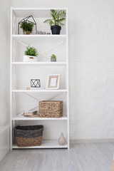 White furniture with shelves and flowers in a bright room with a brick wall.