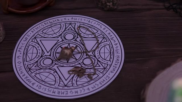 Witchcraft and wizardry. Burning green candle, Astrological pendulum for Tarot and the occult circle for fortune-telling next to magic potions and subjects. Low light, close-up