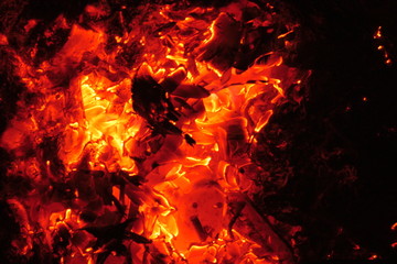 The fire charcoals of a bonfire glow in the night with red heat. Abstract dark and red-orange background.