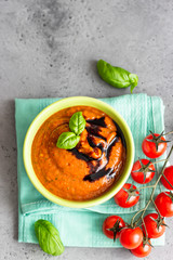 Tasty appetizing summer tomato soup puree gazpacho garnish with balsamic sauce and basil in bowl. Grey stone background. Top view.