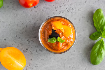 Delicious gazpacho soup in glass. Traditional spanish cold soup puree gaspacho garnish with tomato, cucumber and basil. Grey concrete background.