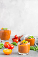 Delicious gazpacho soup in glass. Traditional spanish cold soup puree gaspacho garnish with tomato, cucumber and basil. Grey concrete background.