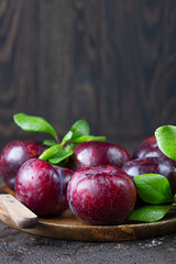 Purple plum with leaves on wooden plate and knife, dark background. Autumn harvest.