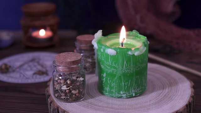 Witchcraft and wizardry. Burning green candle and magic potions next to Astrological pendulum for Tarot and the occult circle for fortune-telling next to magic subjects. Low light, close-up