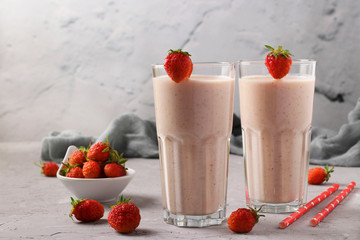 Two servings of homemade protein cocktail with fresh strawberries and yogurt in glasses on gray concrete background, Diet and weight loss control concept, Copy space