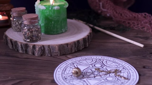Witchcraft and wizardry. An astrological pendulum for Tarot and an occult circle for divination next to burning green candle, magical potions and subjects. Low light, close-up