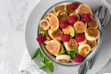 Bowl with tiny pancake cereal with raspberries, mint and jam on a light grey concrete background. Trendy food. Pancake porridge.