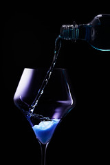 Blue drink is poured into a glass. Black background.
