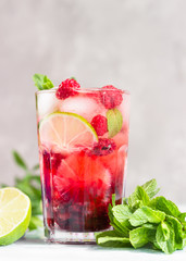Lemonade or non-alcohol cocktail with raspberry, lime and mint in glass on grey background. Summer berry drink.