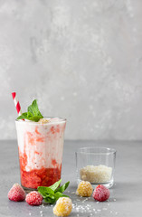 Layered strawberry and raspberry smoothie or milkshake in glasses decorated with mint, raspberry and coconut flakes. Healthy food for breakfast or snack.