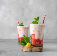 Strawberry and raspberry smoothies in glasses garnish with mint and raspberry on wooden cutting board. Grey background.