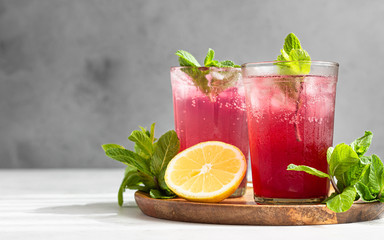 Cold sparkling hibiscus or karkade tea with lemon, mint and ice in glasses on a grey stone...