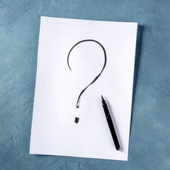 Question mark, written in ink on a piece of standard office paper, overhead square shot on a blue...