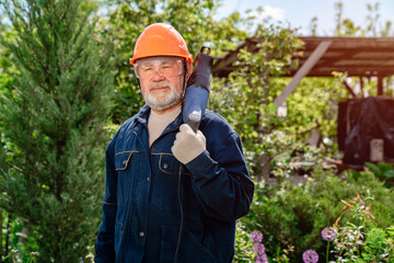 elderly man with beard in hardhat and glasses with reciprocating saber saw. 