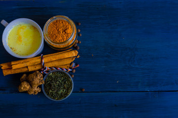 Golden milk powder and a glass with golden milk, on a blue table.
