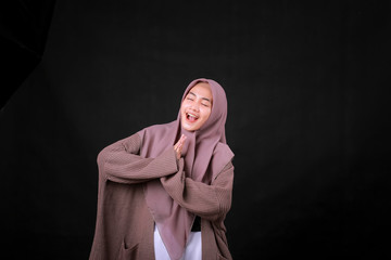 Young Asian Islam woman wearing headscarf gives greeting hands at with a big smile on her face. Indonesian woman on gray background. Eid Mubarak / Eid Fitr / Eid Al-Fitr greeting